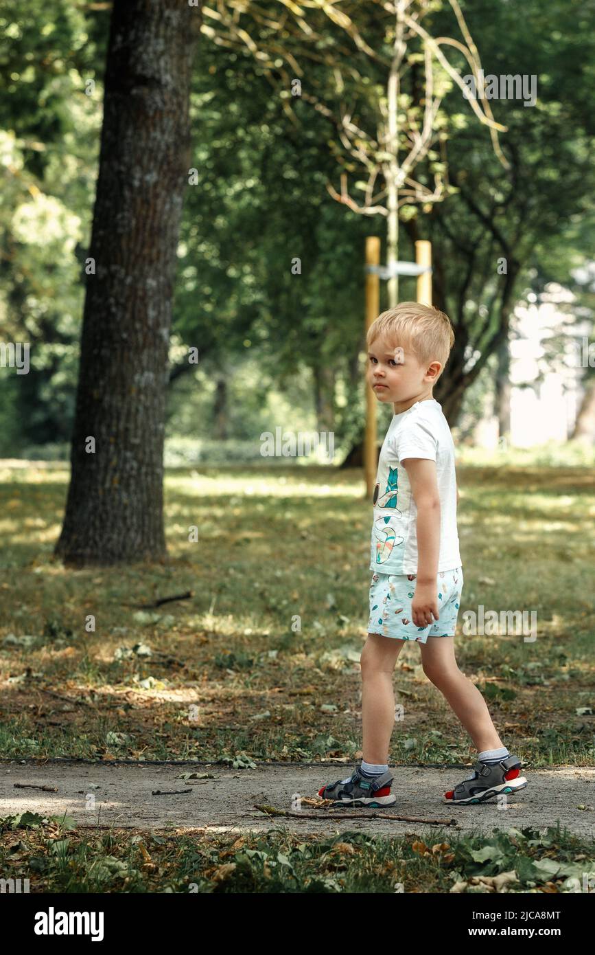 A sad lonely little boy walks in a city park. The child got lost he was looking for his parents. Stock Photo