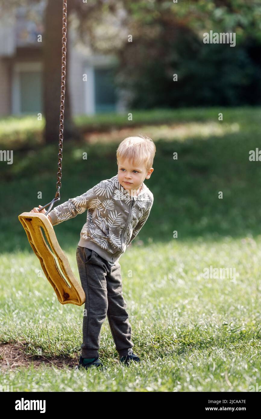 A broken swing in a city park and a cute boy who can't swing. Stock Photo