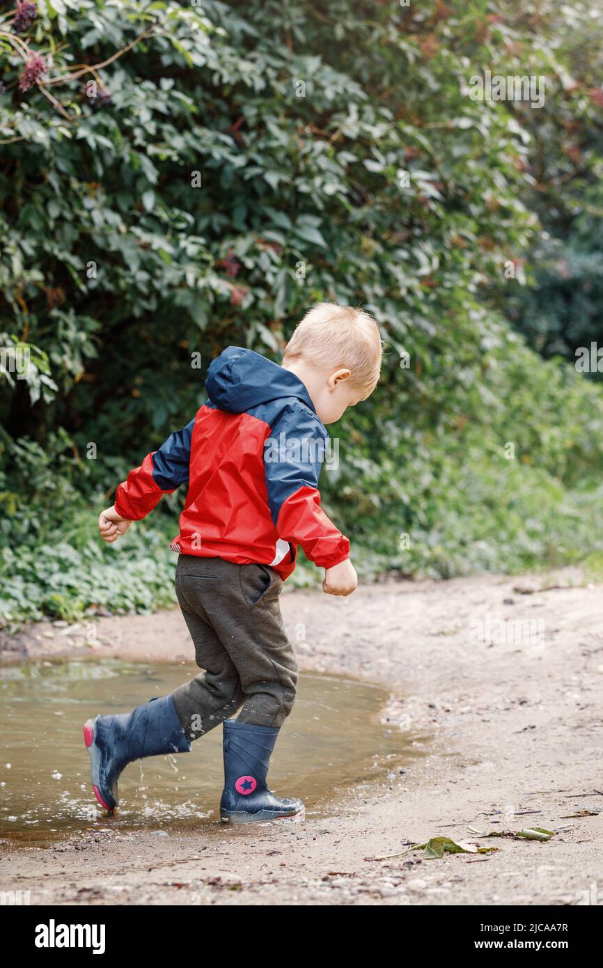 Playful boy splashing water in puddle on road. Stock Photo