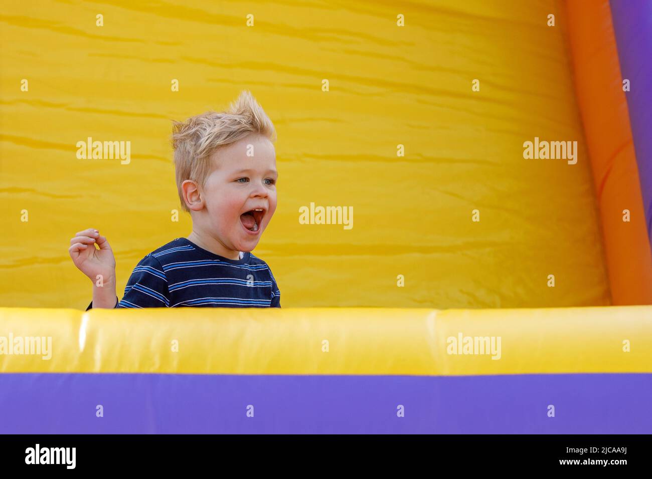 Little boy having fun in inflatable castle playground. Furious child shouts loudly. Bright yellow rubber trampoline background, there is free copy spa Stock Photo