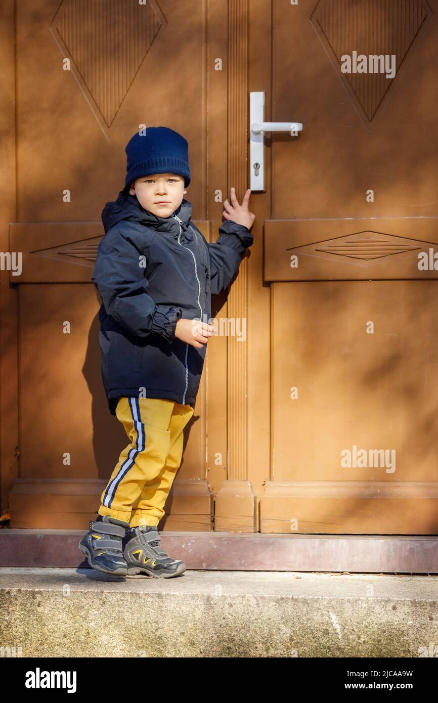 Little boy knocking the brown door in the down city. Stock Photo