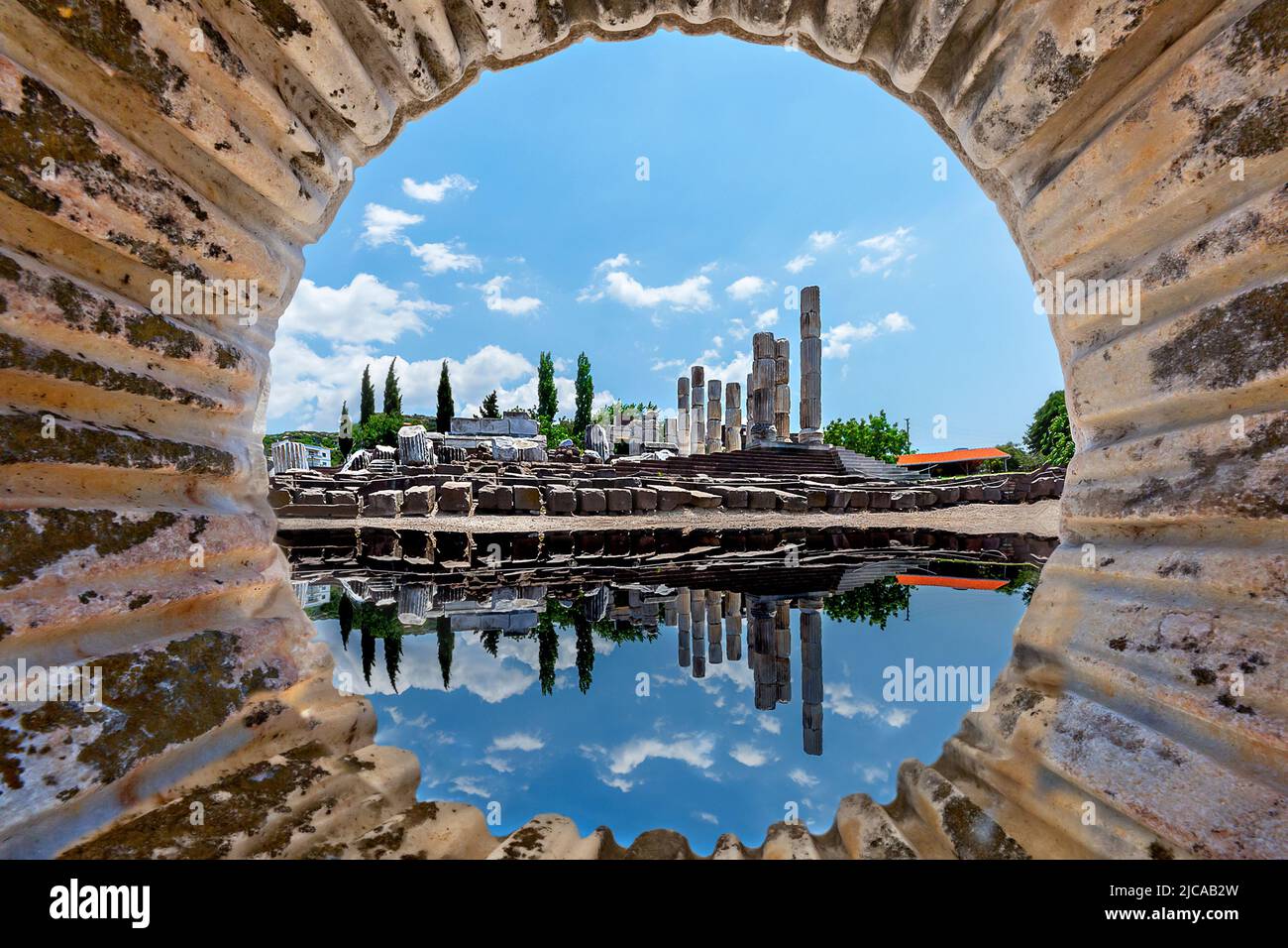 Ruins of the sanctuary of Apollon Smintheus and its reflection in the puddle through the carved out marble column in Ayvacik, Turkey. Stock Photo