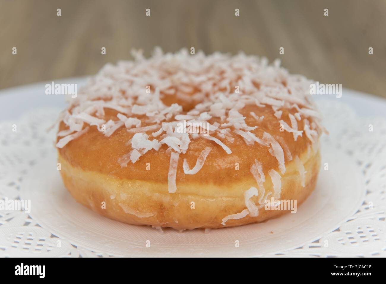 Tempting fresh from the oven coconut glazed donut from the bakery served on a plate. Stock Photo