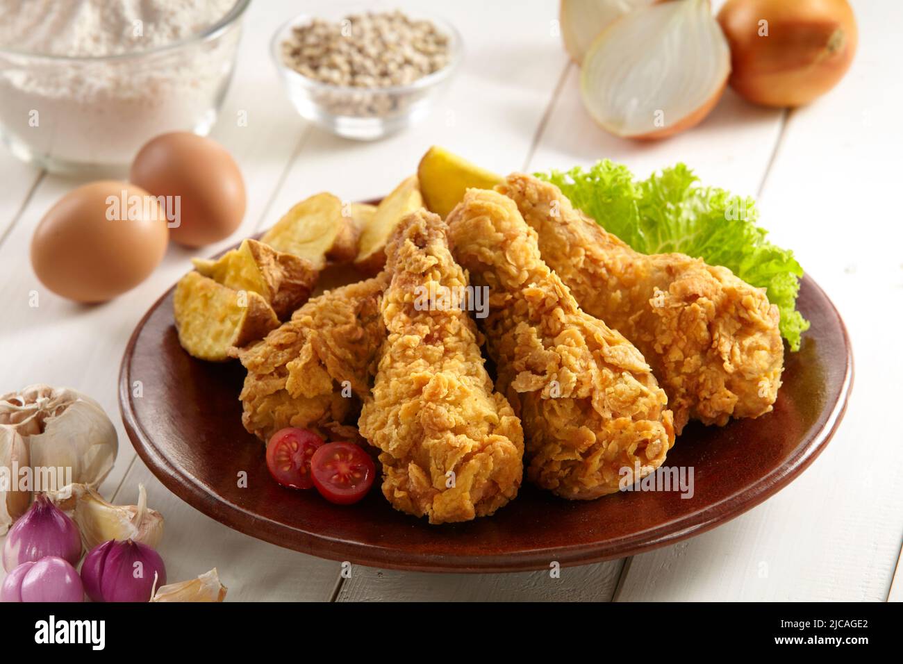 a plate of crispy fried chicken served with potatoes wedges, vegetables and some of the ingredients Stock Photo