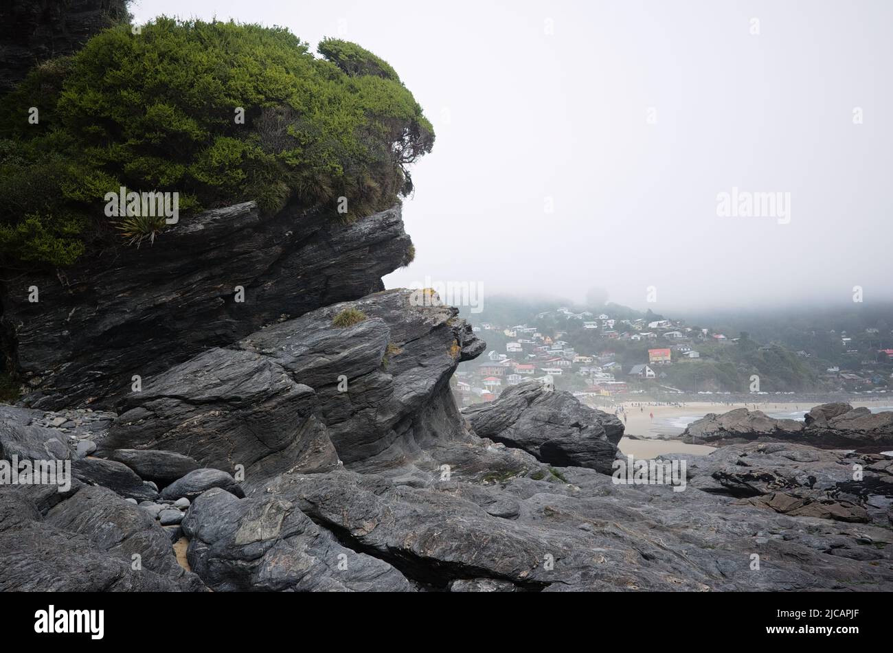 Volcanic rock formation on Pacific coast of Chile, near Maicolpue village, Los Lagos. Playa Rio Sur beach and hills with houses in fog on background Stock Photo