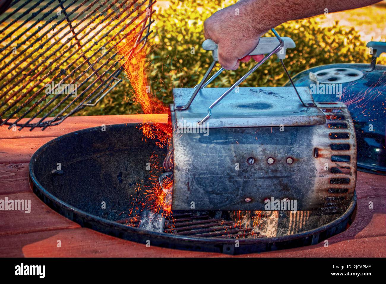 sparks fly out of charcoal lighting chimney with briquettes being poured into kettle outdoor grill. Stock Photo