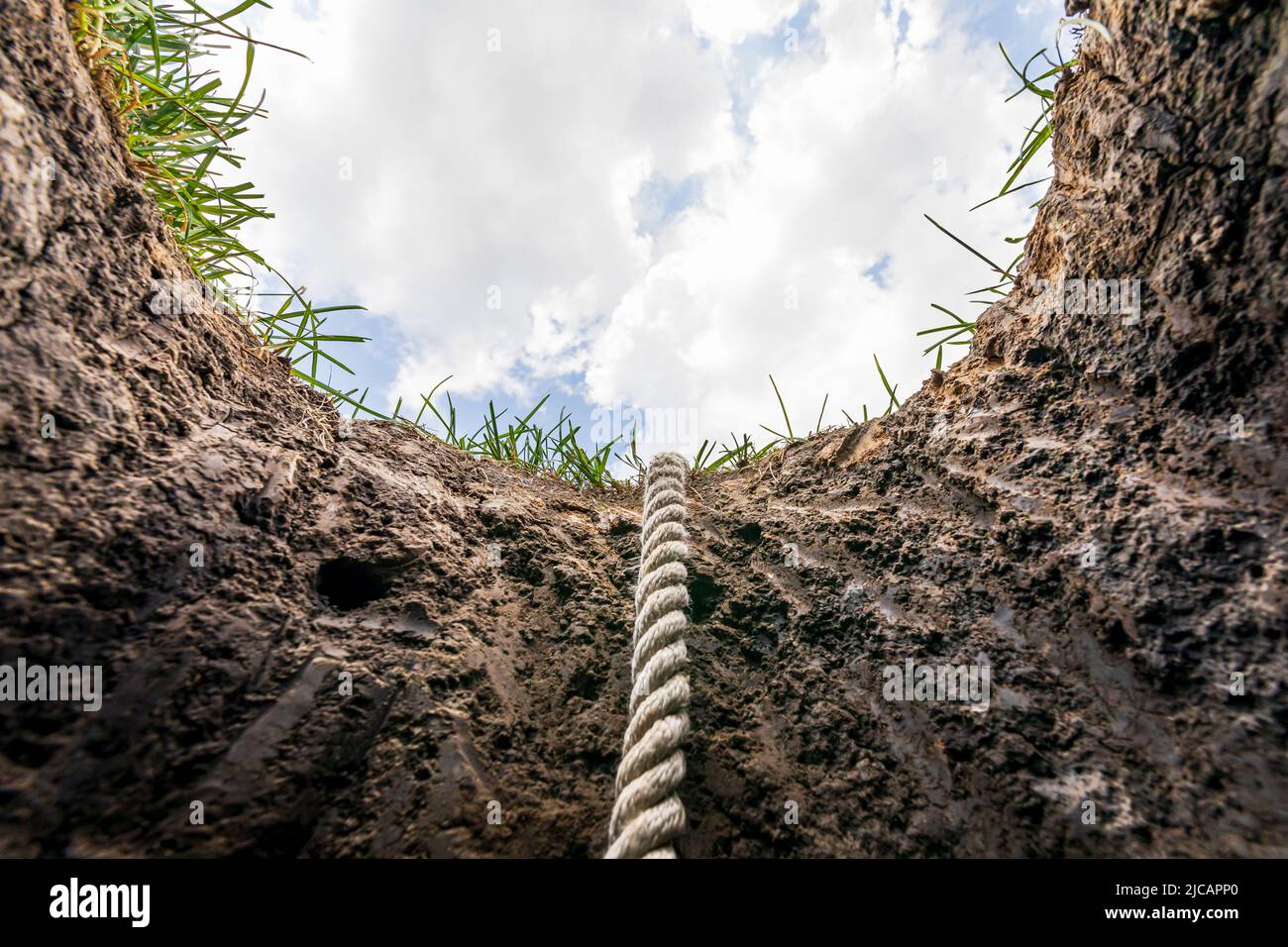 Looking up from hole in ground with rope. Lifeline, debt, mental health help concept. Stock Photo