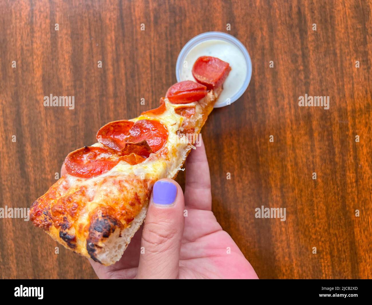 A slice of pizza being dipped in ranch dressing by a man's hand with