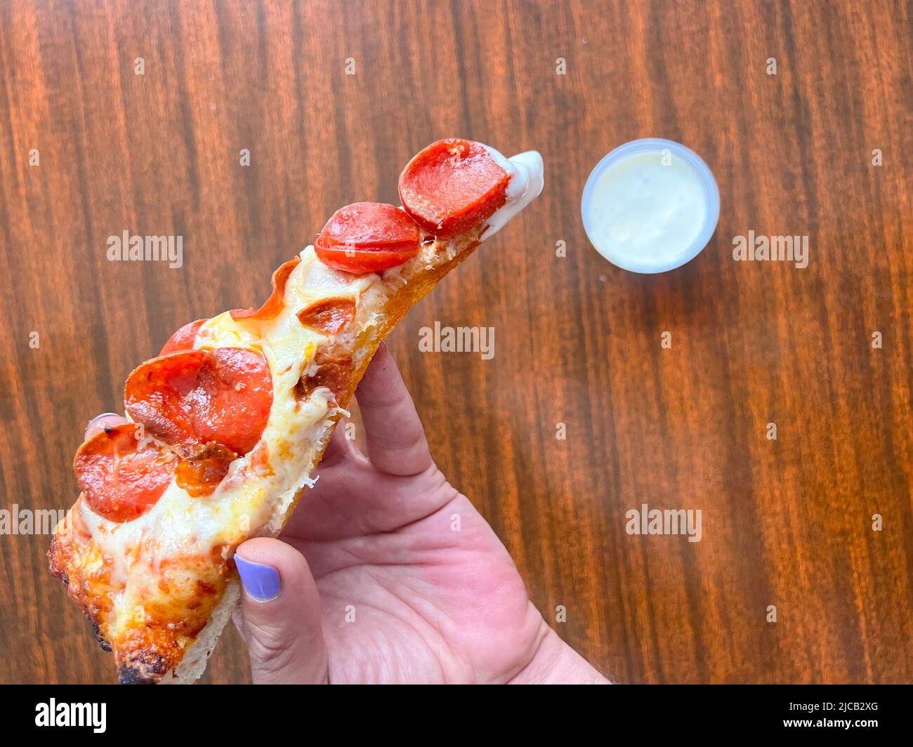 A slice of pizza being dipped in ranch dressing by a man's hand with