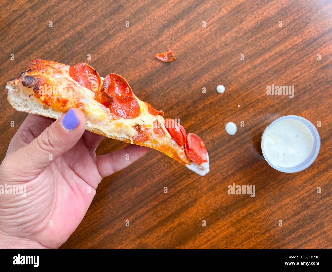 A slice of pizza being dipped in ranch dressing by a man's hand with