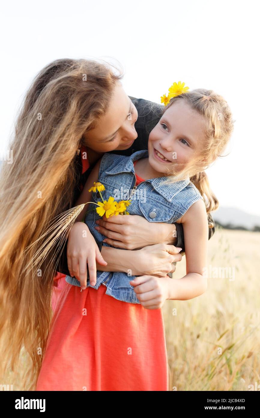 Portrait of a happy young mother and her lovely daughter playing and laughing in a field of wheat . Freedom concept.Mom kissing daughter. Stock Photo