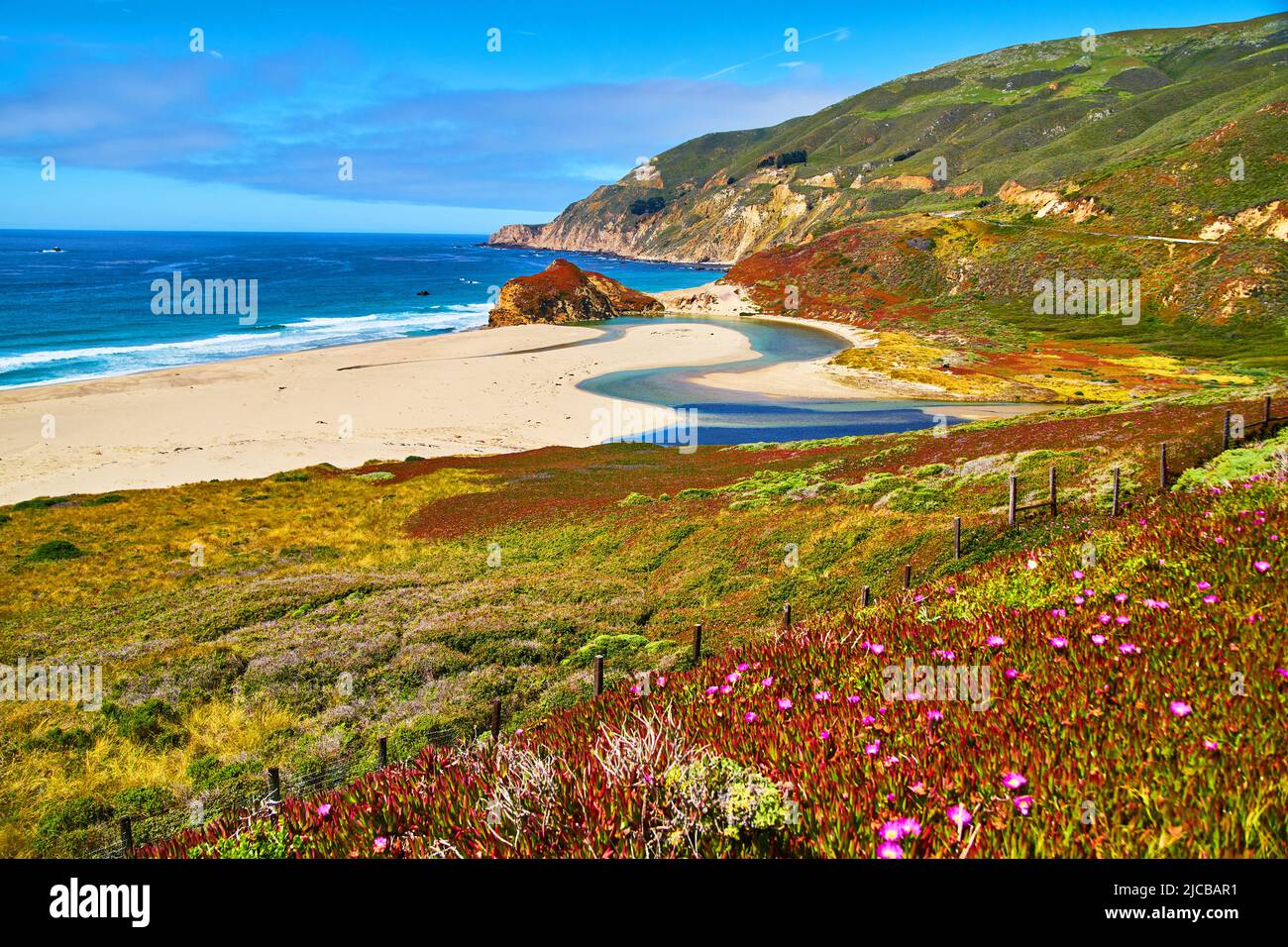 Majestic blue river of water meets the ocean on the beach with fields