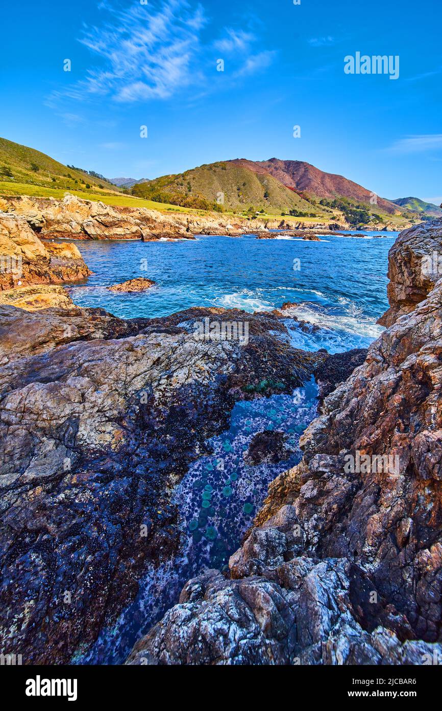 Tide pool hidden by rocks and hit by ocean waves Stock Photo