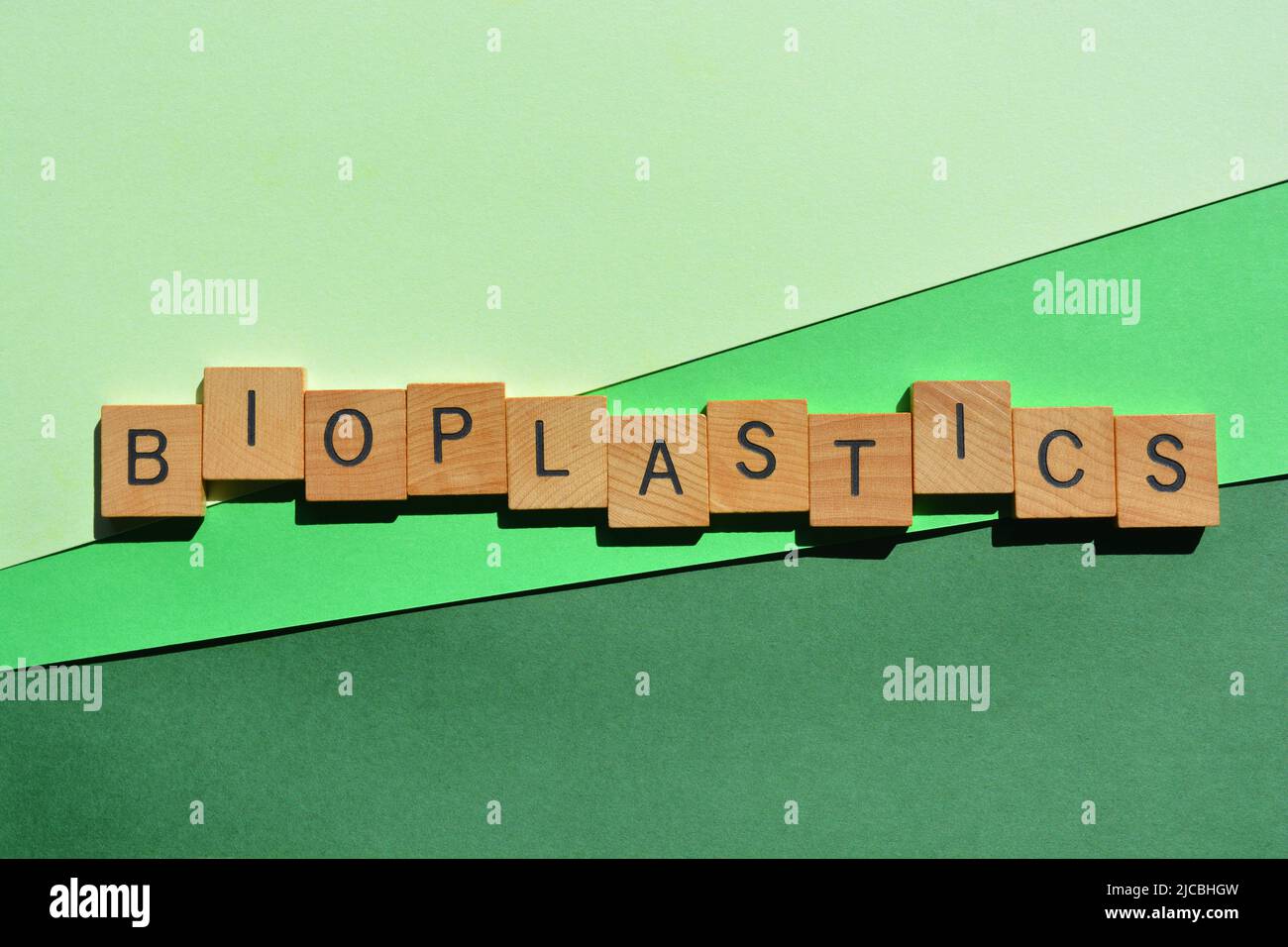Bioplastics, word in wooden alphabet letters isolated on green background Stock Photo