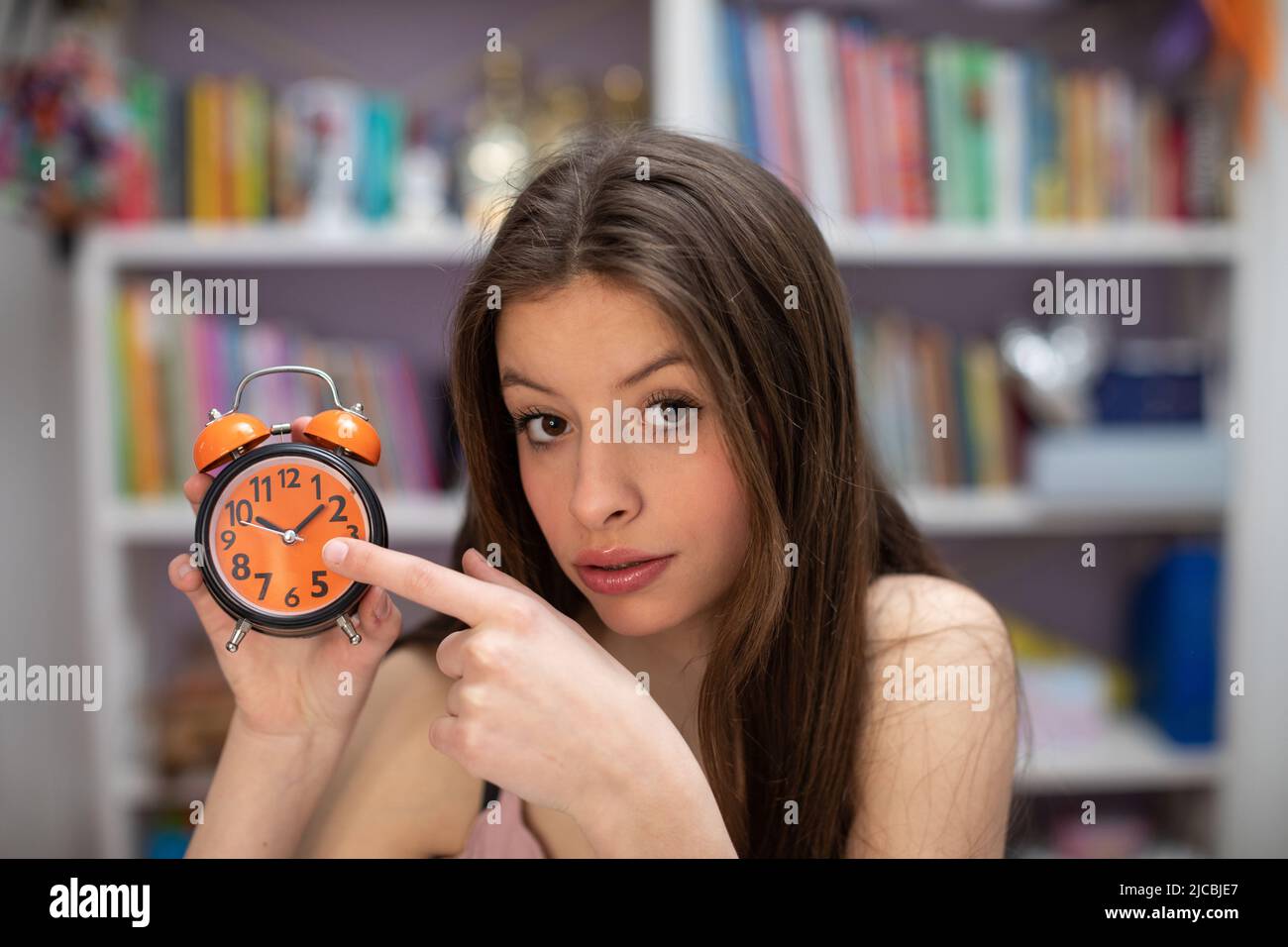 Attractive teenage girl shows off her alarm clock. Closeup view from