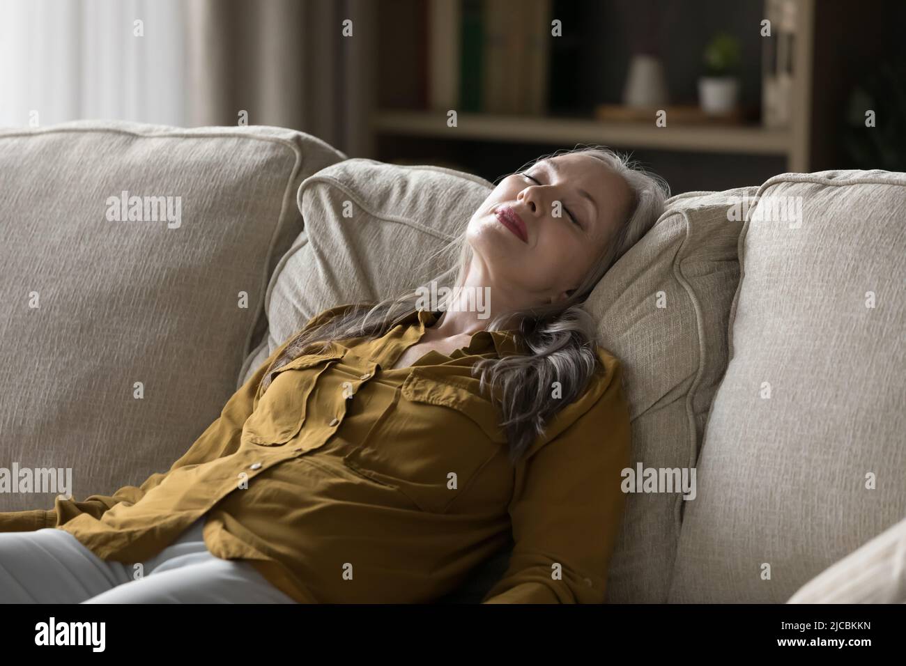 Peaceful middle aged woman sleeping leaned on sofa Stock Photo