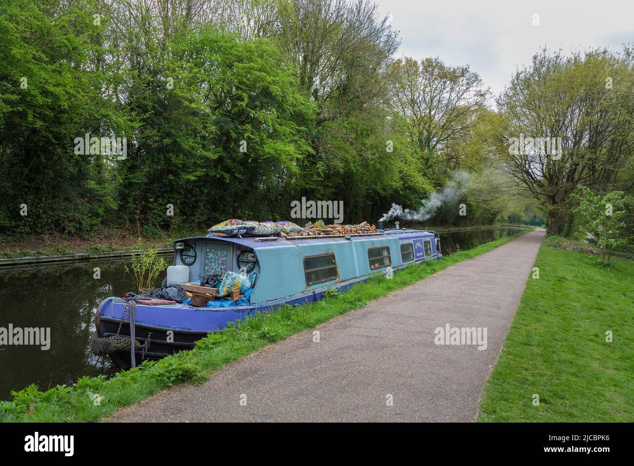 A houseboat or narrow boat moored on a canal with smoke coming from the chimney of a log burning stove. Alternative lifestyle or holiday concept. Stock Photo