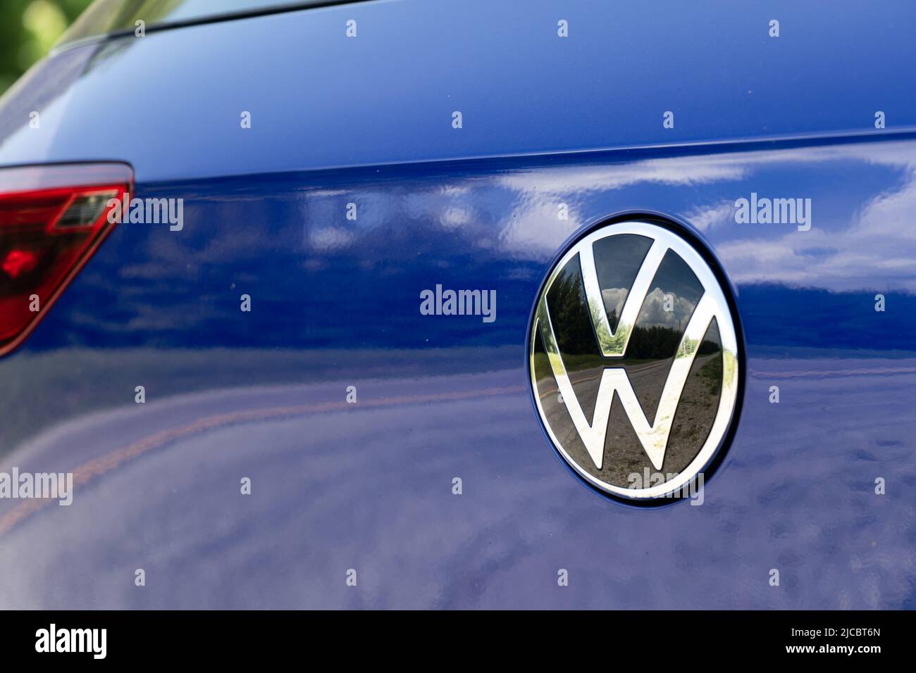 A chrome VW emblem logo is seen on the rear of a new, blue Volkswagen Golf. Stock Photo