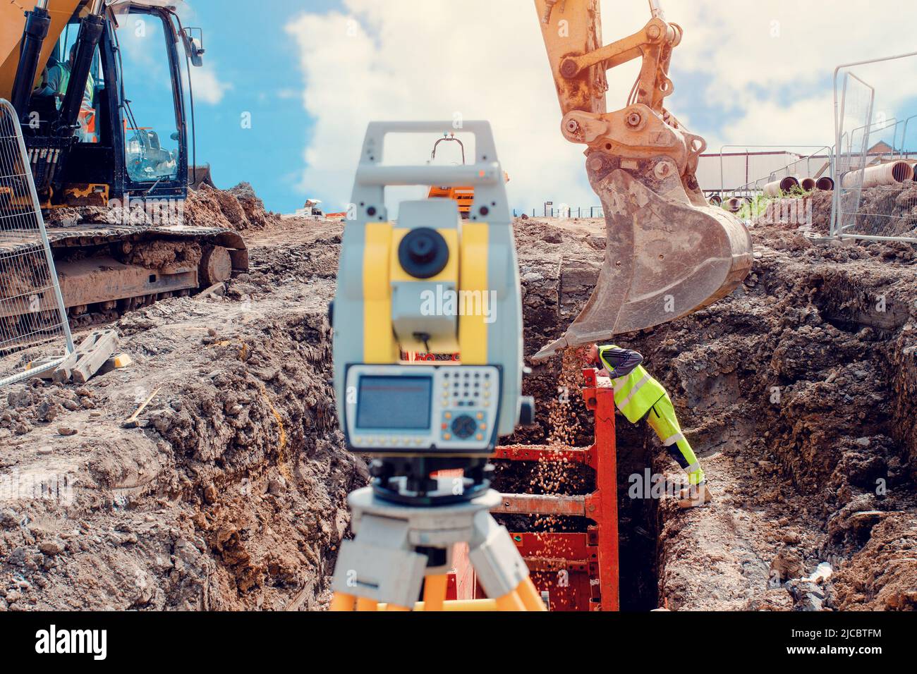 Deep drainage excavation works, with red trench support box installed into the trench and yellow total station next to it Stock Photo