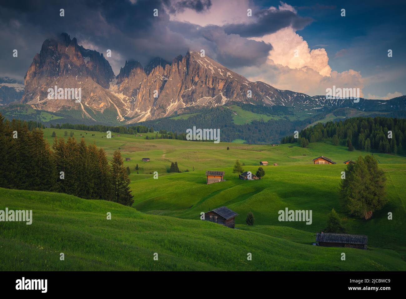 Majestic summer landscape with wooden chalets on the green meadows and snowy mountains in background at sunset, Alpe di Siusi, Dolomites, Italy, Europ Stock Photo
