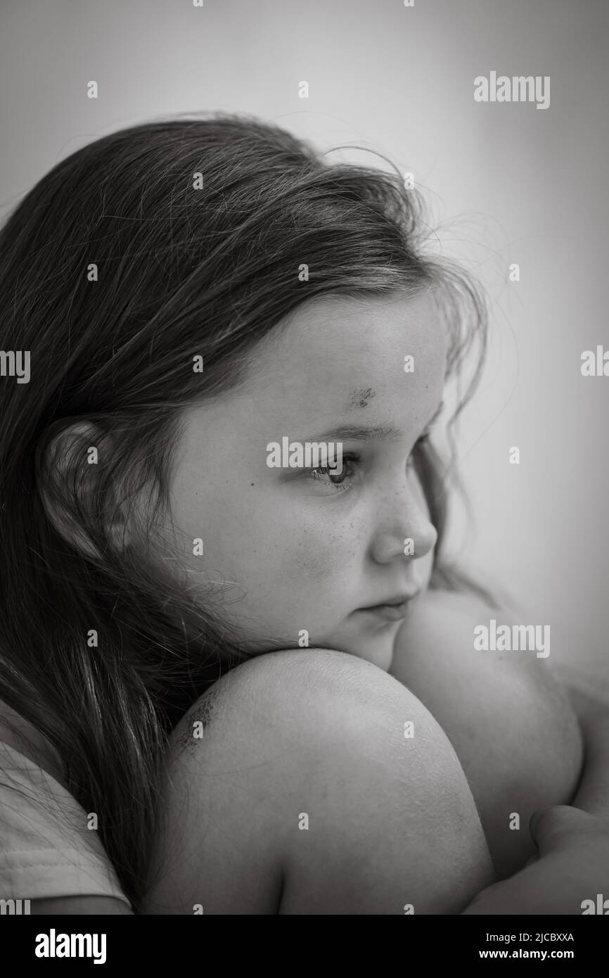 Black and white portrait of little sad shocked wounded girl sitting, hugging knees. Protest against domestic violence. Stock Photo