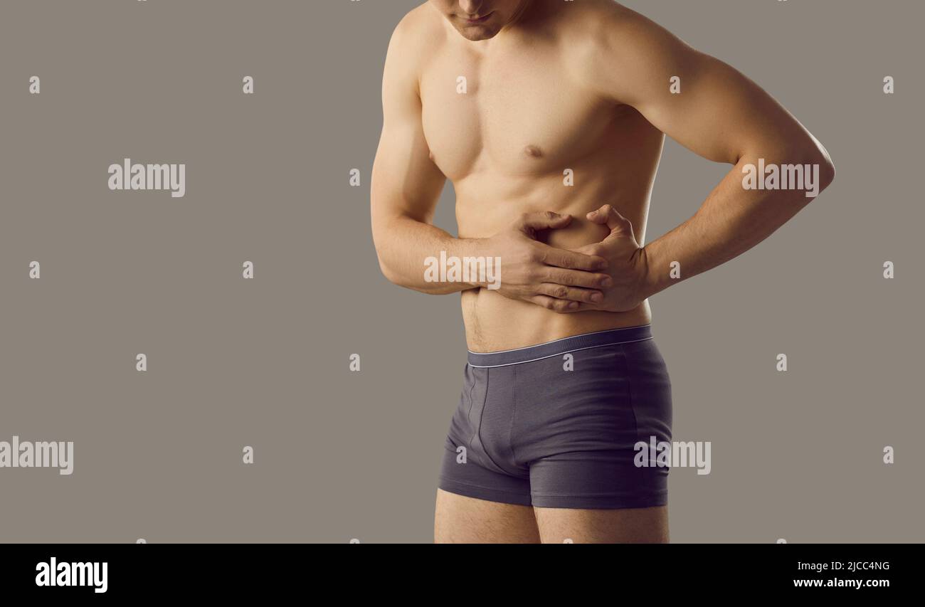 Young muscular man experiencing liver pain standing near copy space on gray banner background. Stock Photo