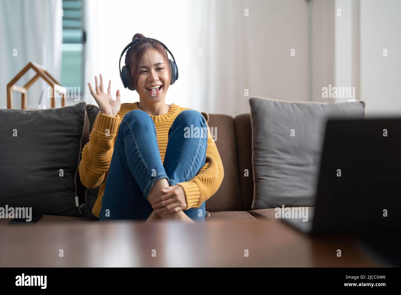 Positive cheerful asian girl have online video call broadcast meet bloggers say hi wave hand sit table use laptop in house indoors. Stock Photo