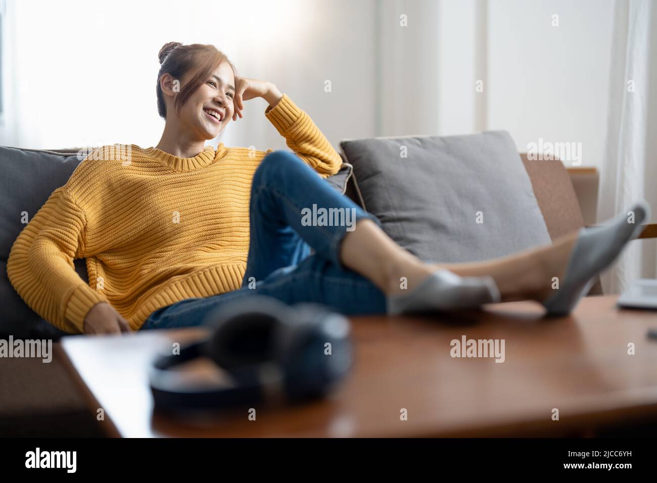 Relaxing home lifestyle happy asian woman in relax room sofa lying back with arms behind head smiling. Asian girl in comfortable lounging chair travel Stock Photo