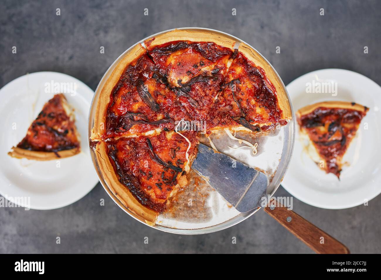 Deep dish pizza with tomato sauce for two person on table in restaurant. Stock Photo
