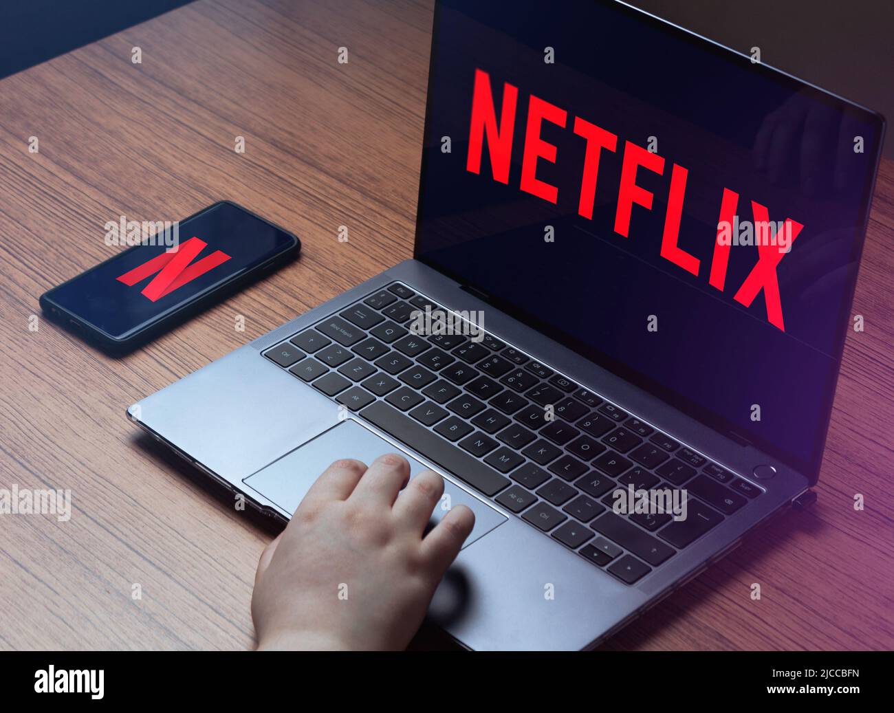 MÁLAGA - SPAIN - MAY 31, 2022: Young woman watching Netflix on laptop. Netflix logo on laptop and smartphone screens. Stock Photo