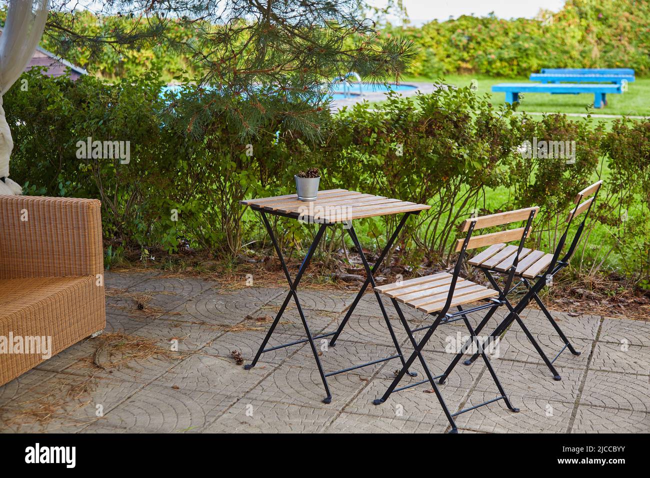 A bucket of pine cones on an empty garden table and two chairs. Empty summer cafe by the pool. End of the season. Quarantine Stock Photo