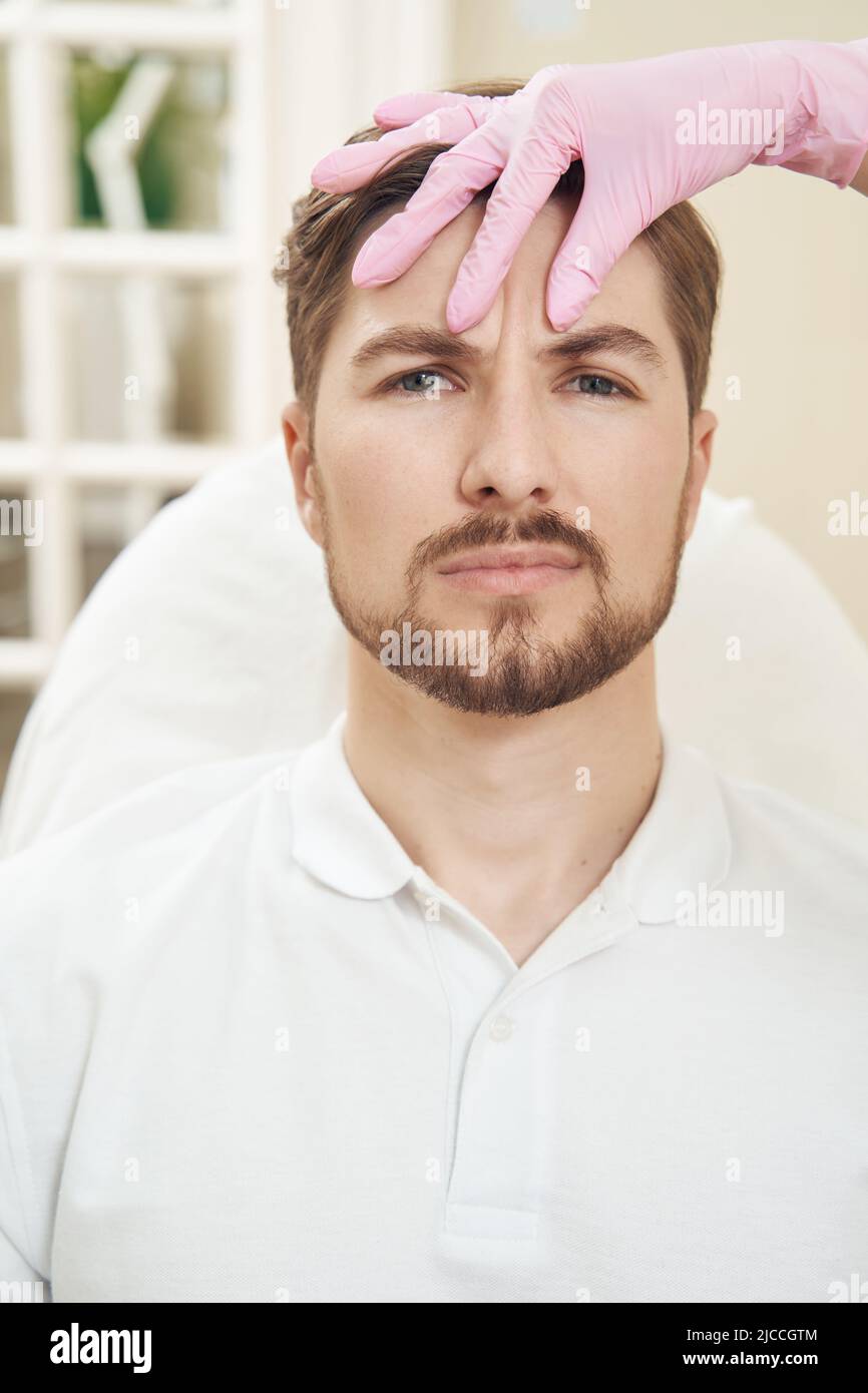 Cosmetologist folding skin on male forehead with fingers Stock Photo