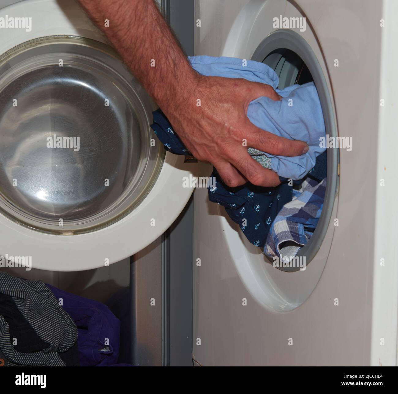 A man's hand putting clothes into a washing machine Stock Photo Alamy