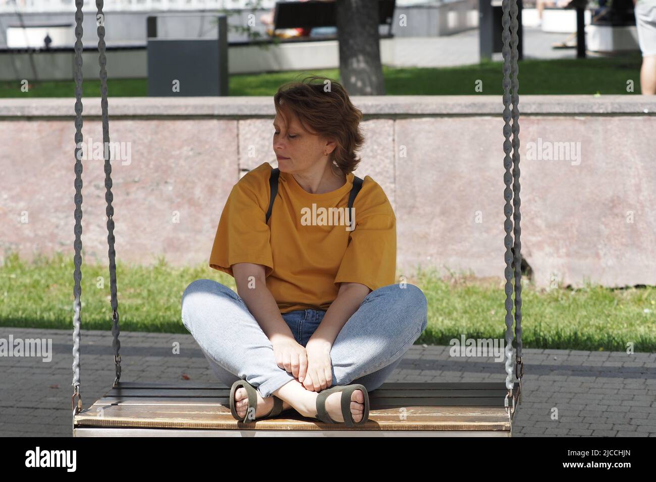 Portrait of a woman. A girl of European appearance in a yellow T-shirt is resting in the park in Stock Photo