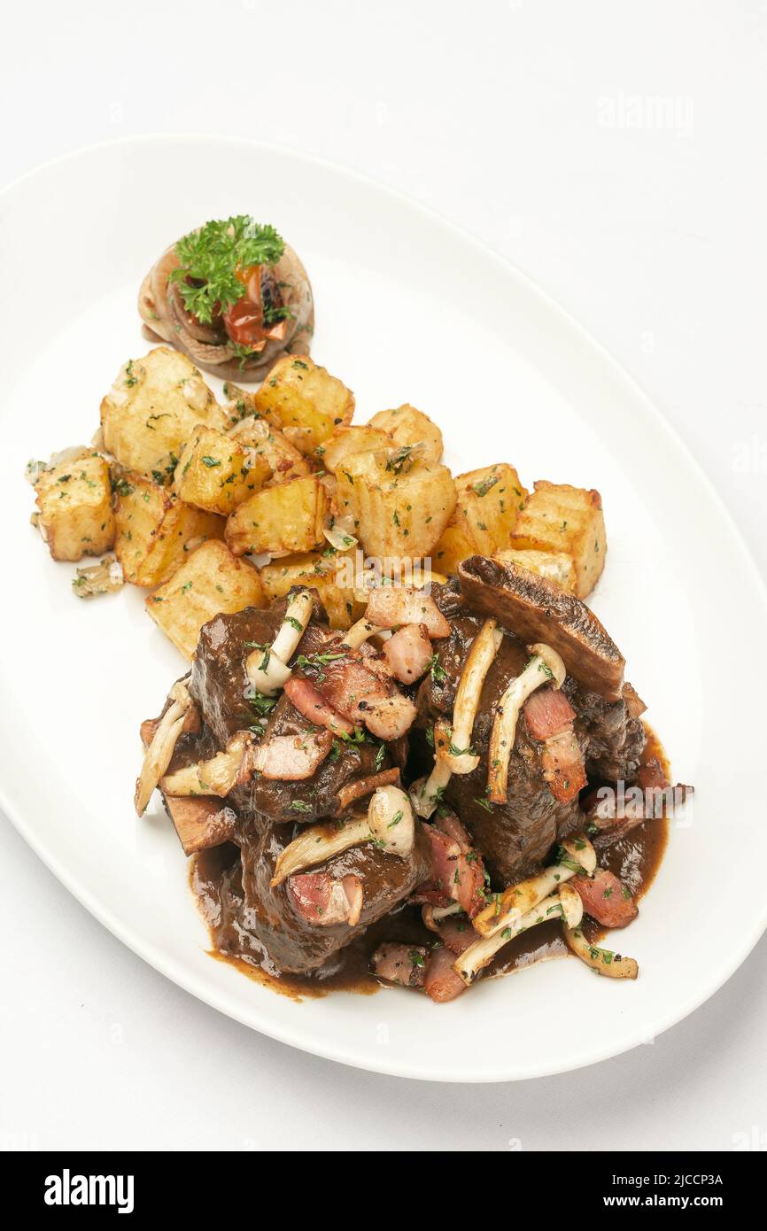 stewed beef short ribs and mushrooms in gravy with roast potatoes on white background Stock Photo