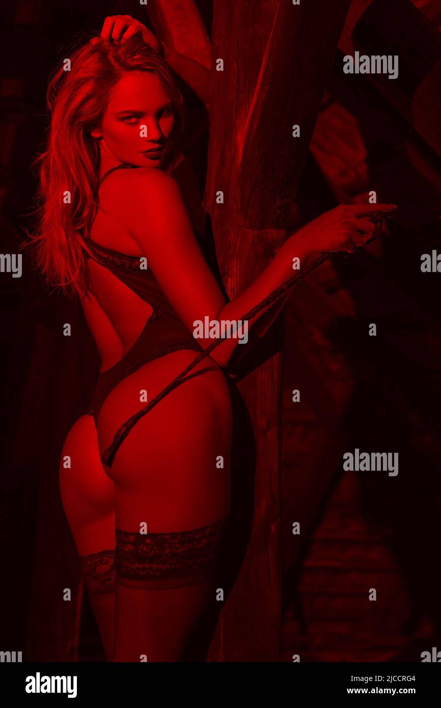 sexy erotic french lingerie Sexy blonde dominatrix in underwear holding whip in underwear at barn in  red light Stock Photo