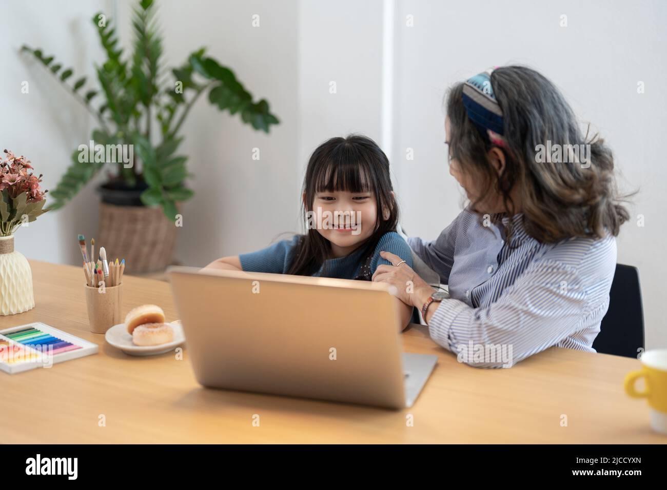 Little girl with grandmother using laptop computer, e learning on virtual online class at home. Stock Photo