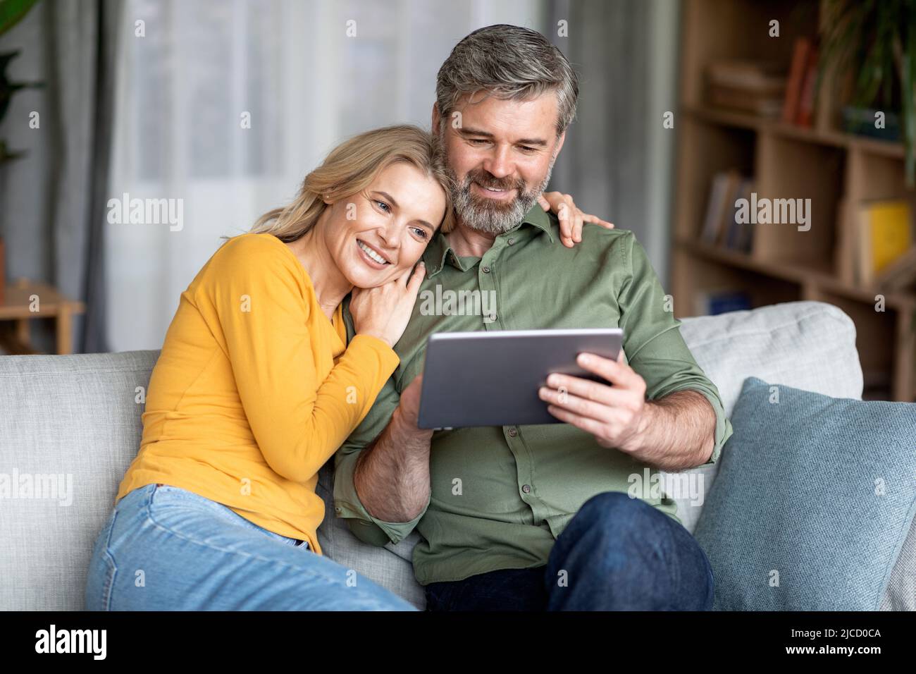 Technologies For Leisure. Happy Middle Aged Spouses Using Digital Tablet At Home Stock Photo