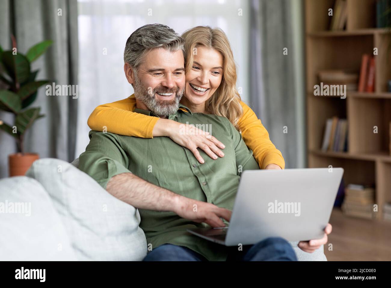 Modern Technologies. Joyful Middle Aged Spouses Spending Time With Laptop At Home Stock Photo