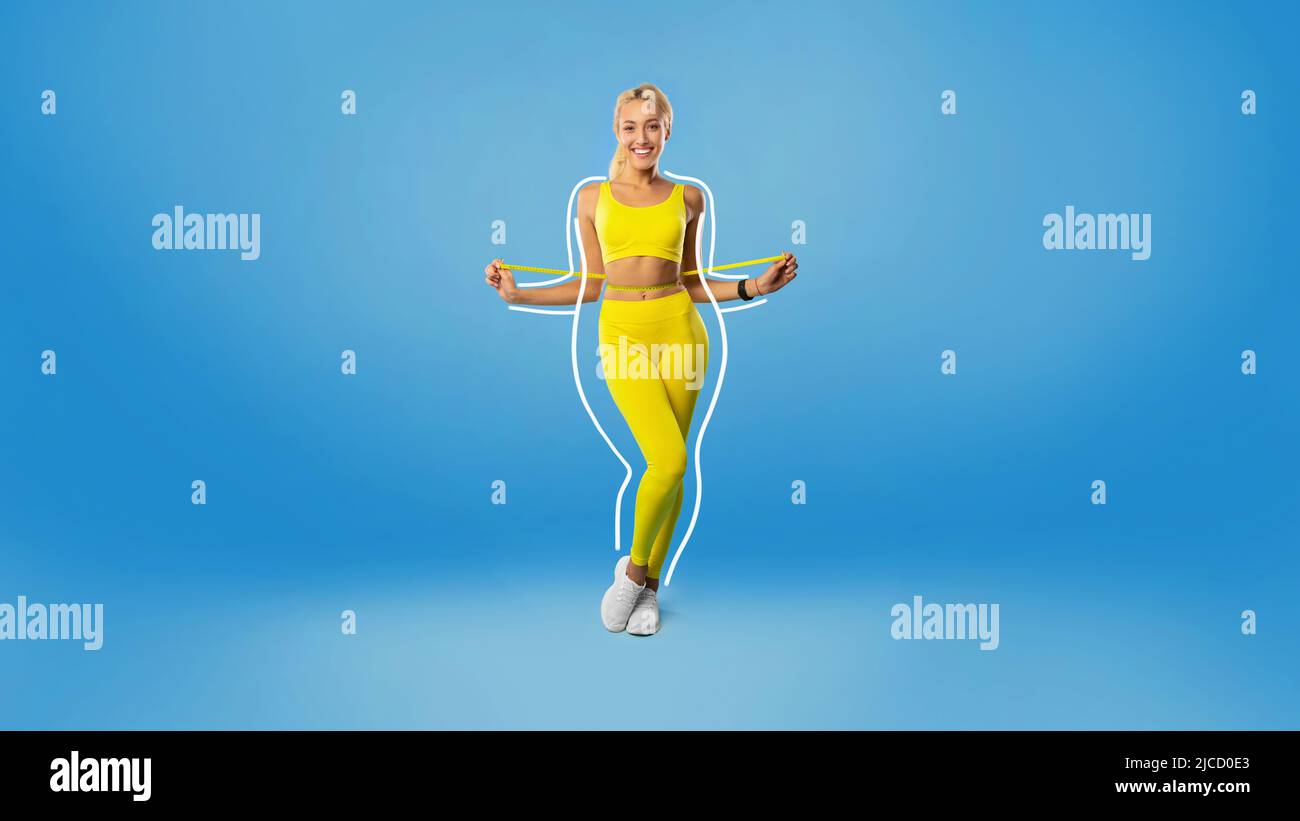 Cheerful young blonde lady in sportswear measuring waist with tape, feeling happy about losing weight on blue background Stock Photo