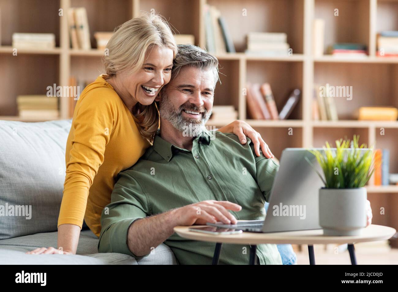 Happy middle aged couple websurfing on laptop together while relaxing at home Stock Photo