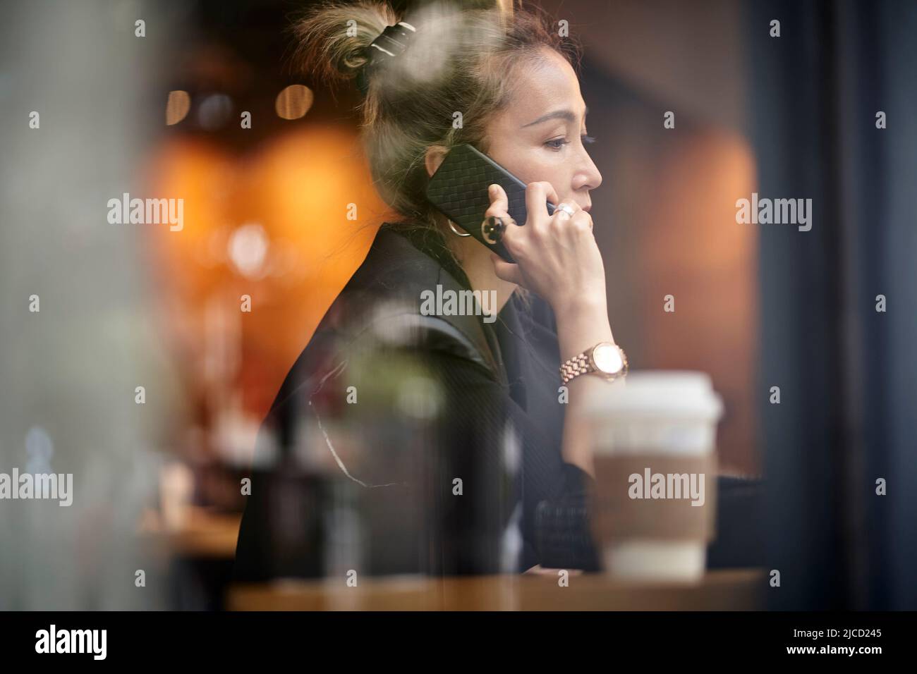 asian woman talking chatting conversing using cellphone in coffee shop Stock Photo