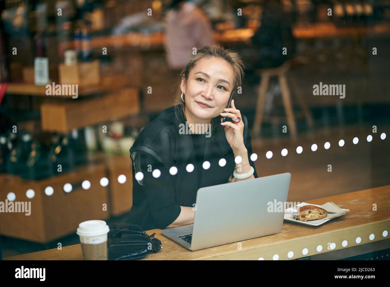 mature asian business woman working in coffee shop using cellphone and laptop computer Stock Photo