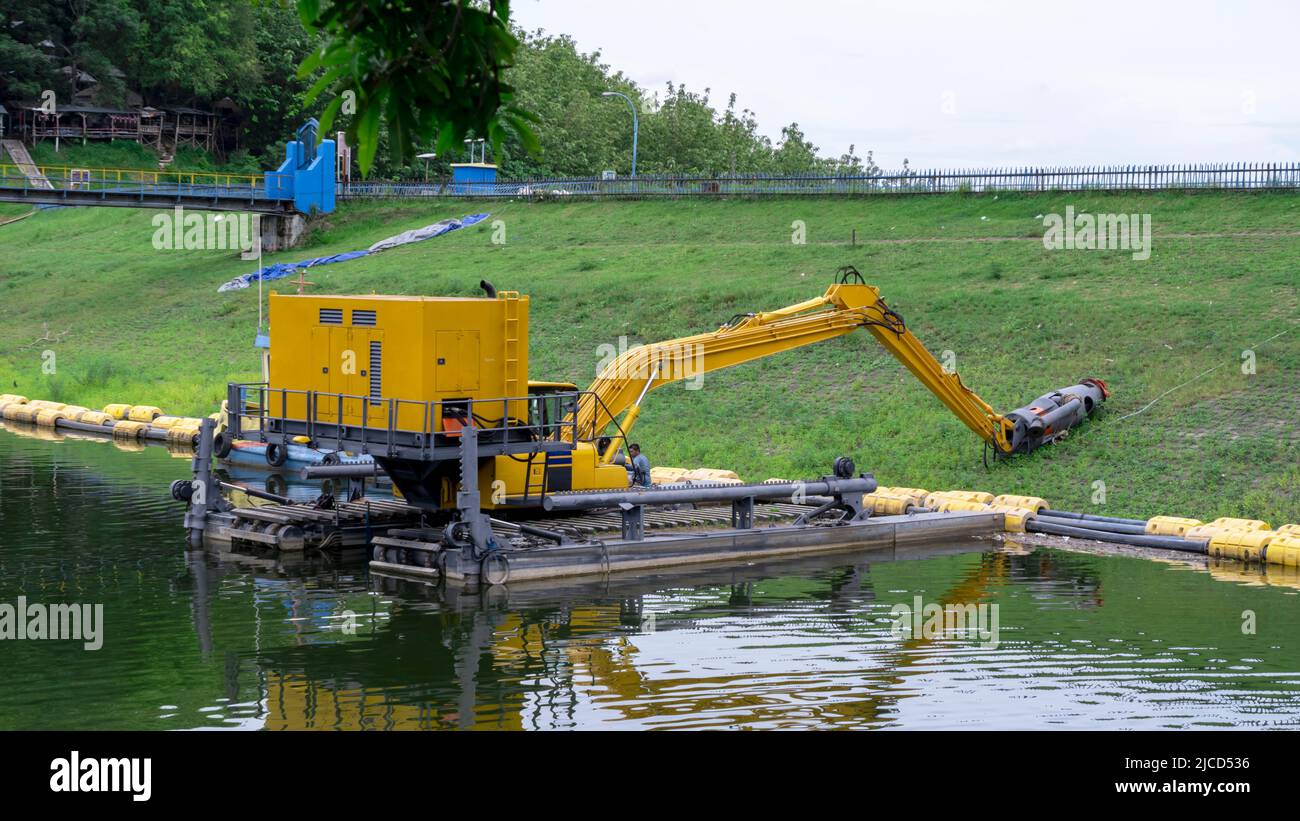 Brebes, Indonesia - Dec 12, 2021: A yellow excavator floating on water. This machine is heavy equipment used in the construction of the Malahayu reser Stock Photo