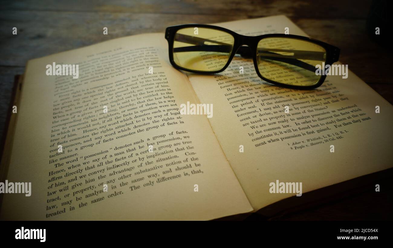 An old book and glasses lie on a wooden table Stock Photo