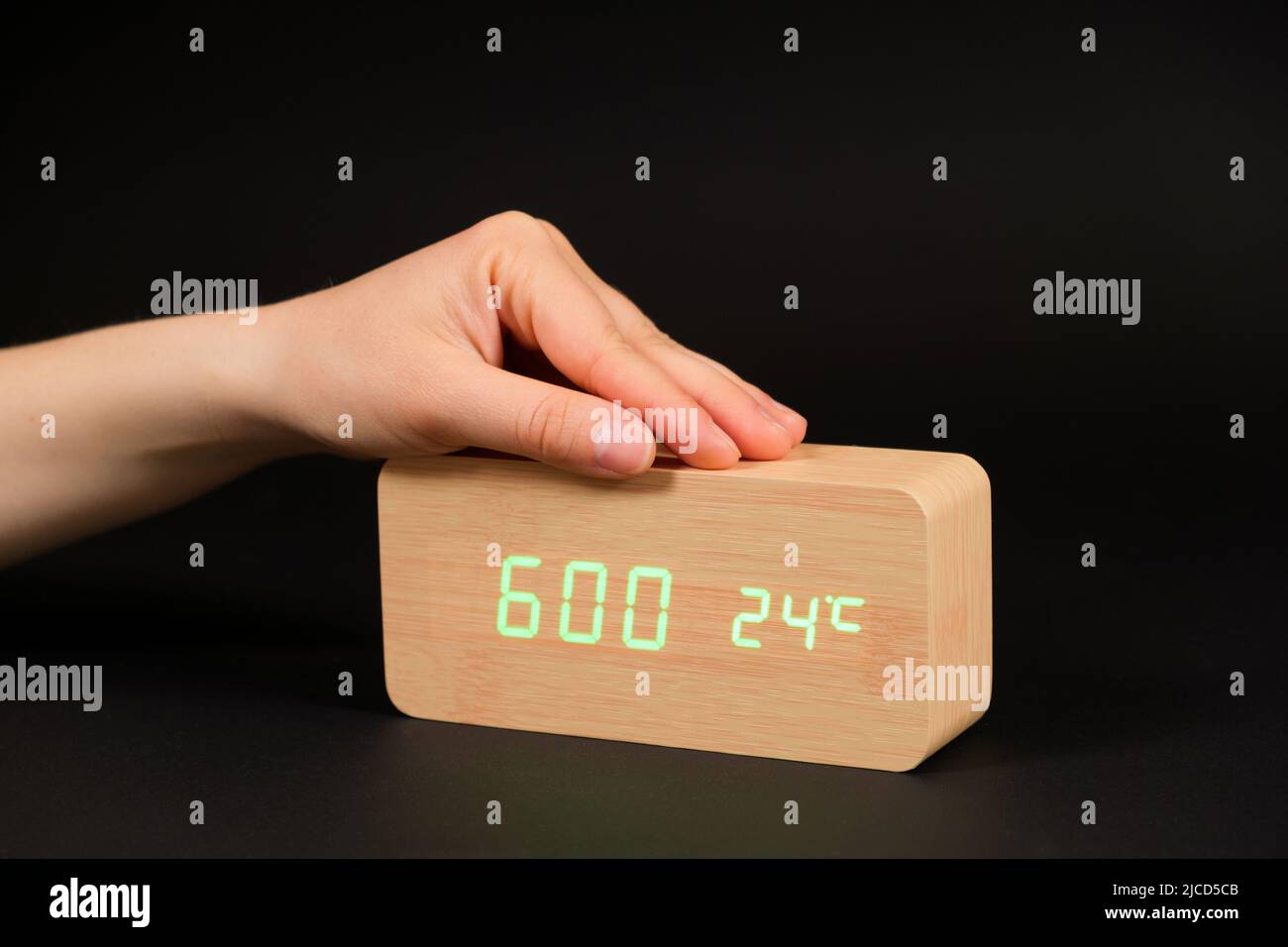 A digital clock showing a time of six o'clock in the morning and a woman's hand on a black