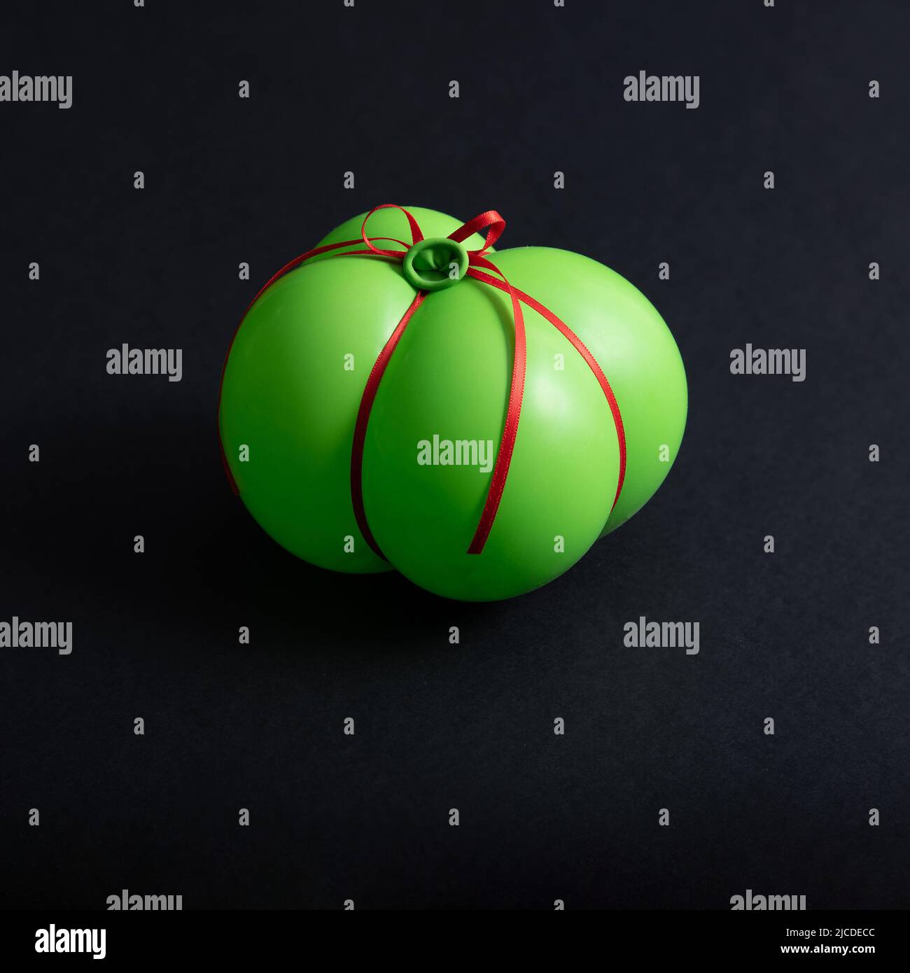 Green party balloon wrapped as a gift isolated on a black background. Minimal abstract concept. Square layout with copy space. Stock Photo