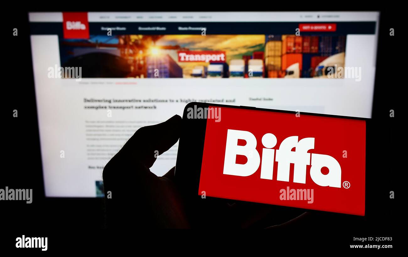 Person holding cellphone with logo of British waste management company Biffa plc on screen in front of business webpage. Focus on phone display. Stock Photo