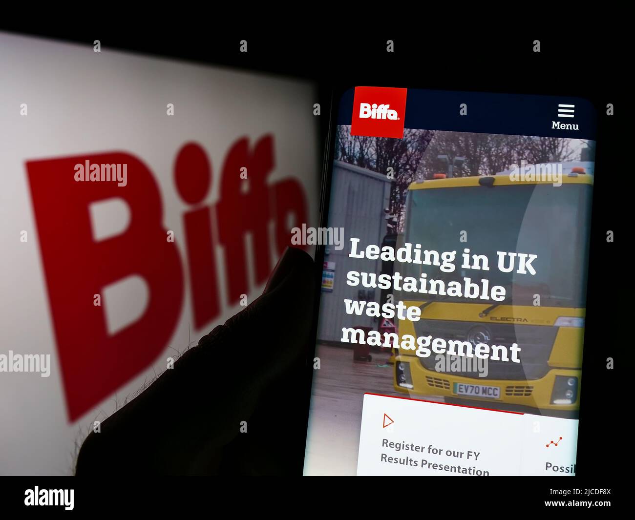 Person holding smartphone with website of British waste management company Biffa plc on screen in front of logo. Focus on center of phone display. Stock Photo