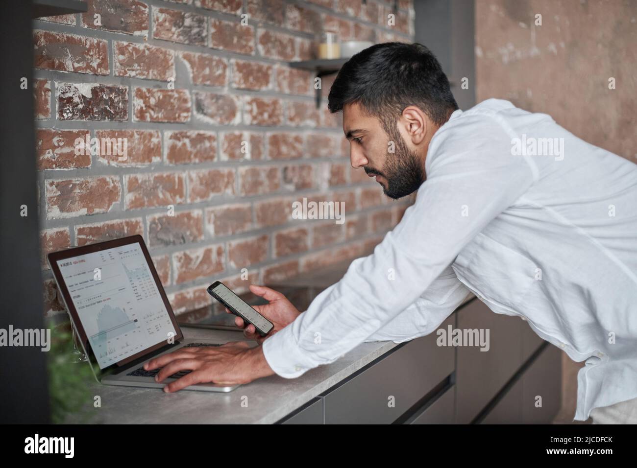young man using a laptop and a smartphone at the same time. Stock Photo
